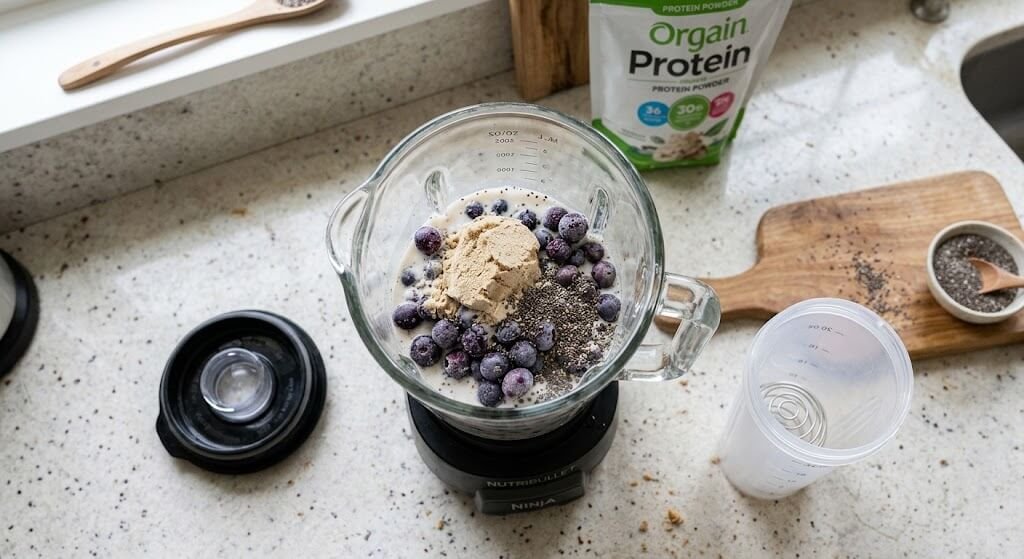 A top-down shot of a blender containing protein powder, chia seeds, frozen blueberries,