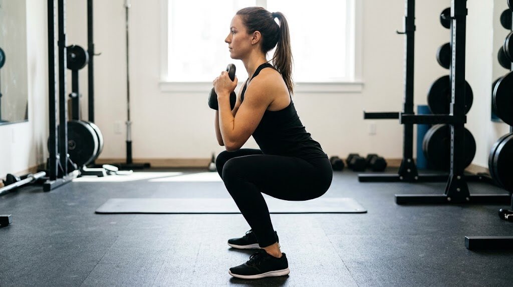 Demonstration of the goblet squat, side view, showing a tall chest, elbows inside the knees, and flat feet